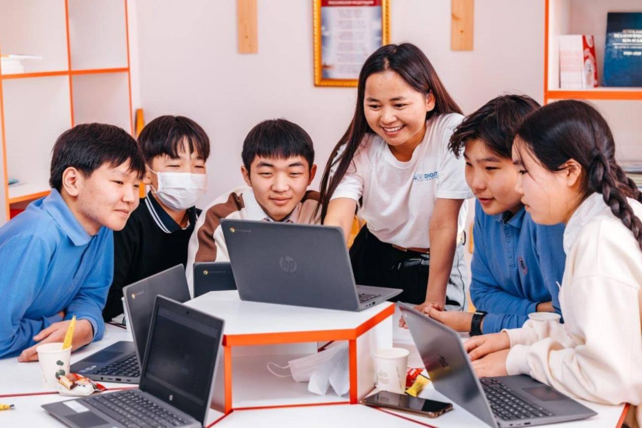 一群面带微笑的小学生围着一位指着电脑屏幕的教师。一群面带微笑的小学生围着一位指着电脑屏幕的教师。